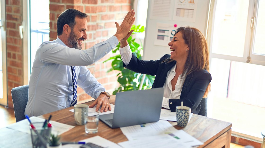 Two colleagues celebrating with a high five at a meeting table