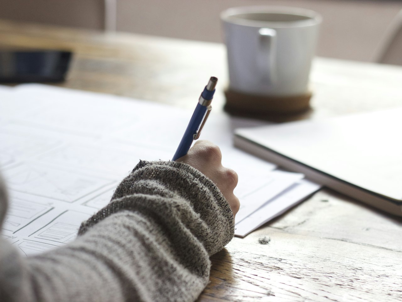 Person writing in a notebook beside a cup of coffee