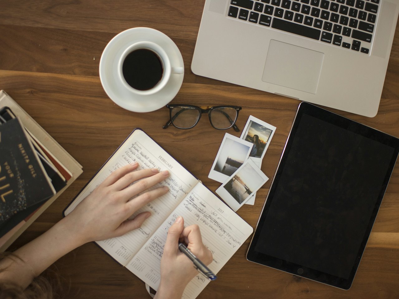 Learner taking notes at a desk next to a laptop and a cup of coffee