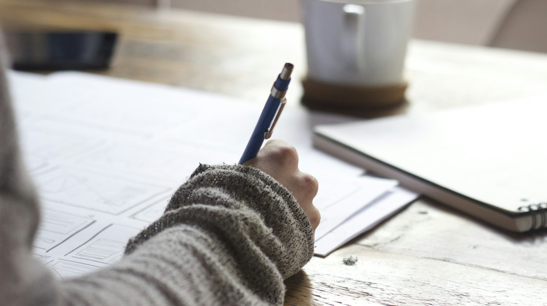 Person writing in a notebook beside a cup of coffee