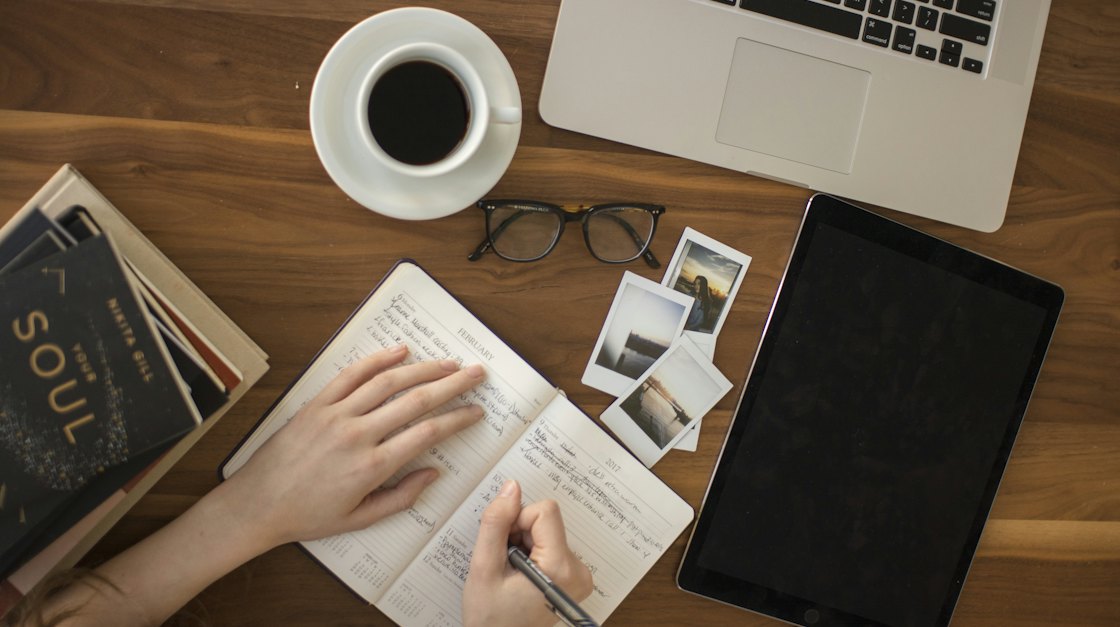 Learner taking notes at a desk next to a laptop and a cup of coffee